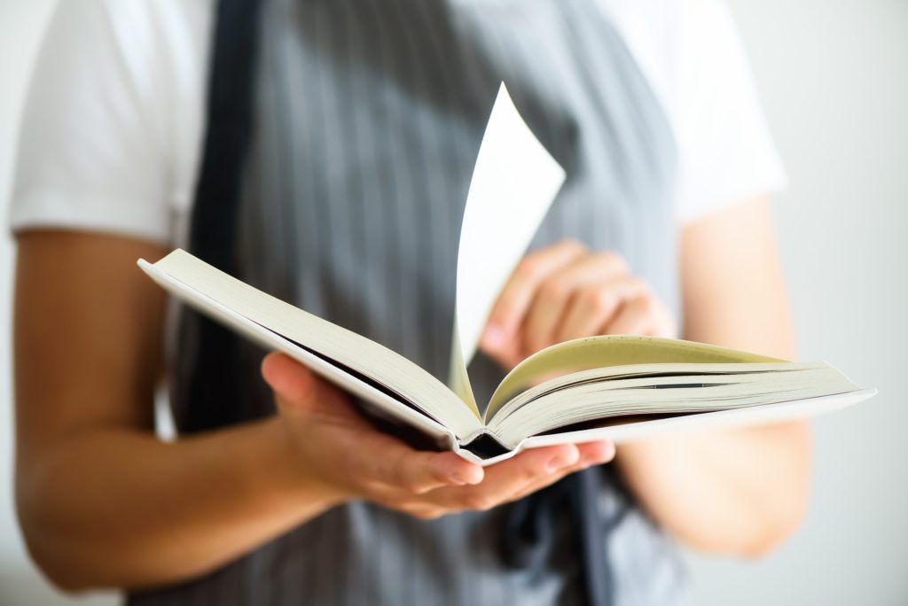 Girl wearing grey apron and reading book. Lifestyle concept